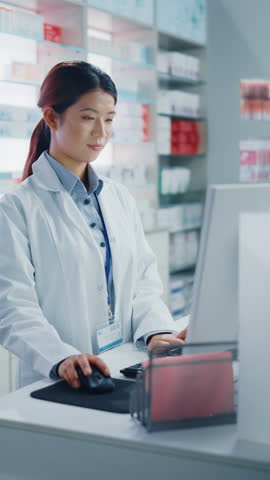 Vertical Screen Video. Pharmacy Drugstore: Beautiful Asian Pharmacist Uses Checkout Counter Computer, Does Inventory Checkup, Online Prescription of Medicine, Supplements Looks at Camera Smiling