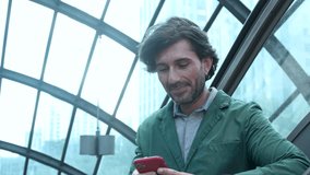 View of young man using a smartphone at twilight in an indoor space in a metro - subway station with a blurred view landscape in the background. High quality video. 
