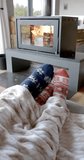 Vertical video of feet of biracial couple sitting on sofa in front of fireplace at home, slow motion. Lifestyle, relaxation and domestic life, unaltered.