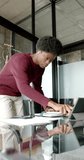 Vertical video of african american man using tablet and taking notes at home, slow motion. Communication, business, remote working and domestic life, unaltered.