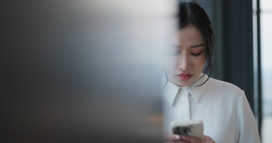 Worried Asian businesswoman checking her smartphone with a hand on her forehead, expressing stress or bad news. Royalty-Free Stock Footage #3463637535