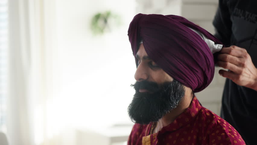 Close up of Indian man tying turban on man head. Video of handsome Indian man with turban.
