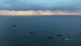 Aerial cinematic footage of Vietnamese fishermen's fishing boats at sea on a cloudy morning with a column of rain in the distance. Background for sensational theme.
