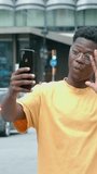 Vertical video.Young african american man making a video call or recording a video with smart phone in a city