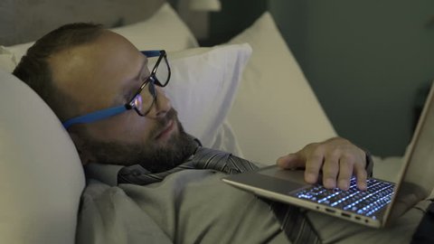 Tired businessman with laptop sleeping on bed in hotel room and waking up