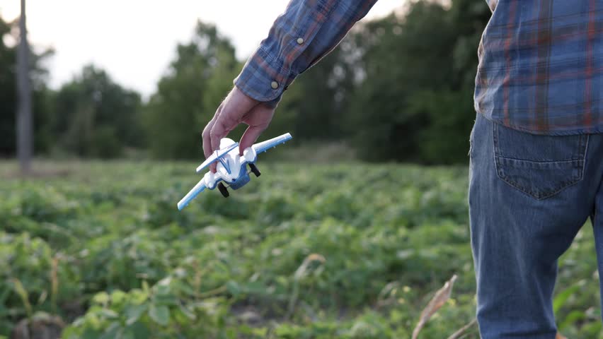 On an agricultural field, a guy holds a model airplane in his hand. A man dreams of becoming an airplane pilot.