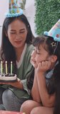 Vertical clip. Mother gives birthday cake to her lovely daughter. Mother and little daughter celebrate a birthday party together at home.