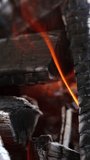 Wooden embers in flame. Smoldered black logs burning out in fire. Background of charcoals in slight orange flame. Close-up. Vertical video