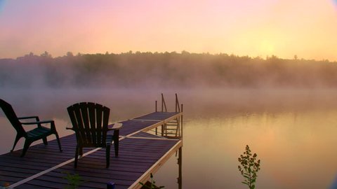 Adirondack chairs on cottage dock overlooking foggy morning lake