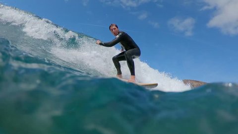 SLOW MOTION CLOSE UP: Enthusiastic surfer riding an epic tubing wave on summer holiday. Man on surfboard carving crystal clear waves in Fuerteventura. Surfer guy surfing in popular surf spot in Lobos.