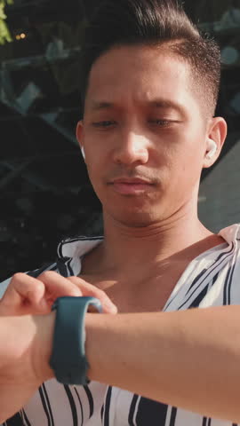 VERTICAL VIDEO: Close-up of young man looking at smart watch
