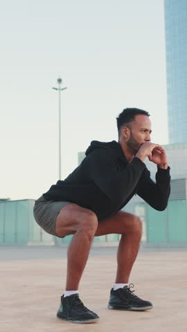 VERTICAL VIDEO: Young bearded male athlete doing workout, squats and jumping on the waterfront Royalty-Free Stock Footage #3463929625