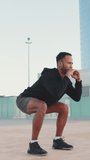 VERTICAL VIDEO: Young bearded male athlete doing workout, squats and jumping on the waterfront