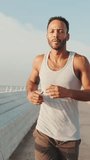 VERTICAL VIDEO: Young bearded male fit athlete runs along the promenade