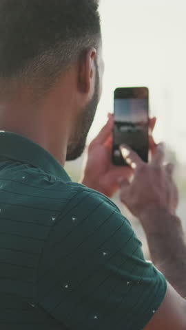 VERTICAL VIDEO, Close up, young man takes photo on smartphone yachts in the seaport. Back view