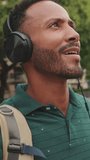 VERTICAL VIDEO, Close up, young man tourist walks around the square of the old city, listens to music in headphones, puts his hands to the headphones