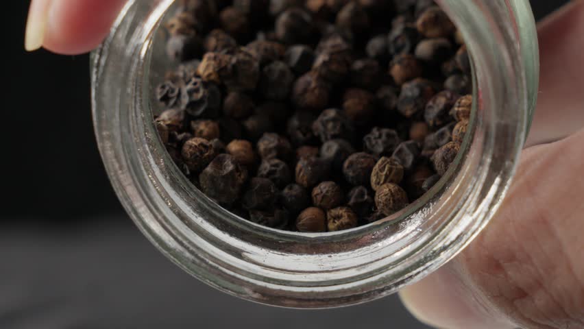 Person Pouring Dried Whole Black Peppercorns. - close up shot