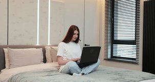 Woman using laptop, working from home in bedroom. Female using laptop at home video chatting with friend. Education, modern tech, e-learning remotely concept.