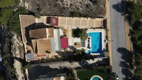 Straight down aerial drone footage of a beautiful house in the town of Benidorm in Spain showing the two story Spanish house with a swimming pool on a hot day in the summer time