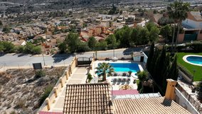 Aerial drone footage of a beautiful house in the town of Benidorm in Spain showing the two story Spanish house with a swimming pool on a hot day in the summer time