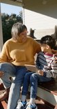 Vertical video of biracial grandmother and grandson sitting on terrace using tablet, slow motion. Family, togetherness, communication and lifestyle, unaltered.