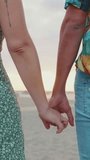 VERTICAL VIDEO: Close up, young couple holding hands on sea background. Back view