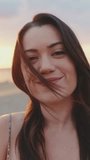 VERTICAL VIDEO: Close up, young woman smiling at camera while standing on the beach