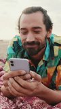 VERTICAL VIDEO: Close up, young happy man using mobile phone on the beach