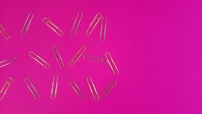 Paper clips on a pink background. Metal paperclips appear and disappear. Stop motion animation.