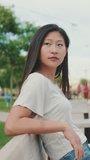 Vertical video, Beautiful brunette girl is resting sitting on bench in city park