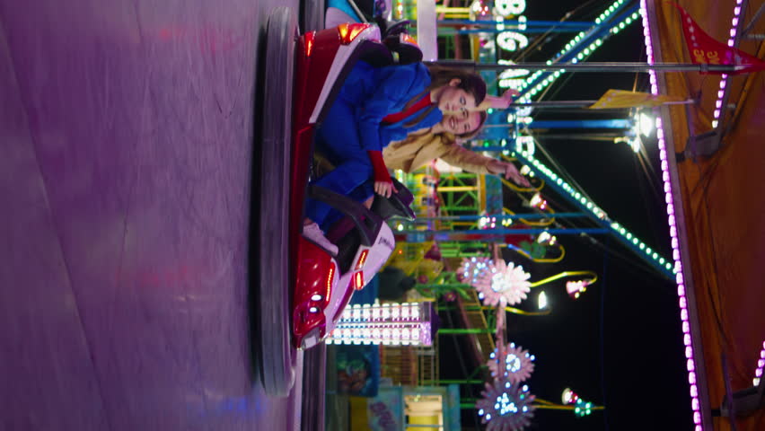 Excited friends driving bumper car in amusement luna park vertical angel. Happy girls enjoying weekend night having fun together. Smiling playful sisters riding dodgem in neon lights. Summer holiday Royalty-Free Stock Footage #3464095737
