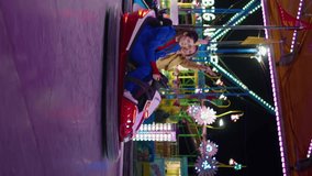 Excited friends driving bumper car in amusement luna park vertical angel. Happy girls enjoying weekend night having fun together. Smiling playful sisters riding dodgem in neon lights. Summer holiday