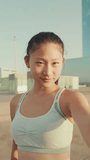 VERTICAL VIDEO, Smiling girl in sports top makes selfie while standing on the embankment in the morning light