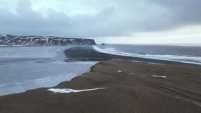 Reynisfjara black sand beach in Iceland with Reynisdrangar cliffs in distance, aerial slide left