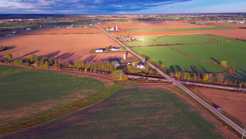 Dazzling Aerial view of country road crossing railroad tracks, through scenic rural agricultural landscape.