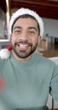 Vertical video of biracial couple wearing santa claus hats having video call at home, slow motion. Lifestyle, christmas, celebration, communication and domestic life, unaltered.