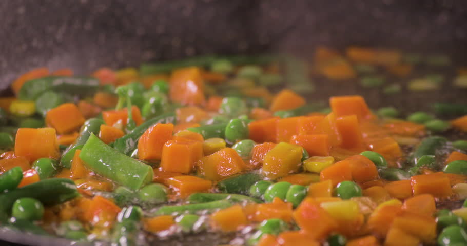 Close up Shot on Mix of Fresh Vegetables in a cooking pan with colorful combination of Green peas and Carrots with a black background and shot on 4K