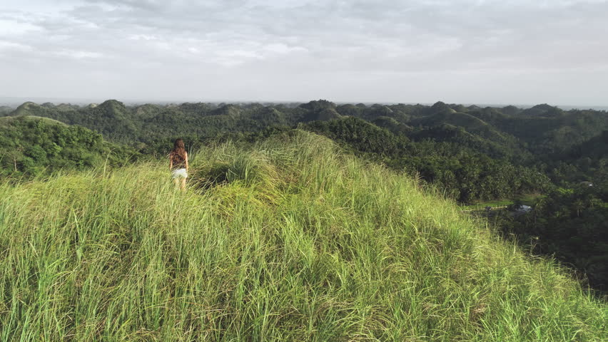 Woman rising up hands aerial view: green grass mount top in tropical Philippines. Traveler girl on hill grassy peak fill freedom of wild asian nature. Epic landcape of exotic mountains in shot 4K, UHD
