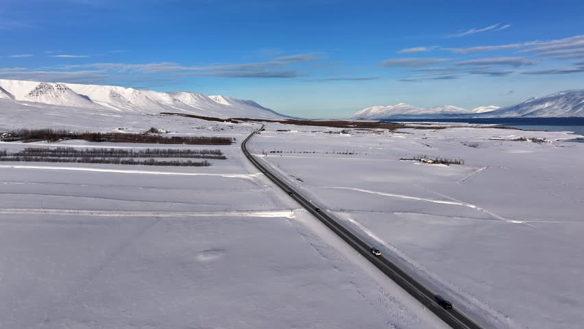 Aerial view of cars driving over a fjord road in Akureyri Iceland on sunny winter day.