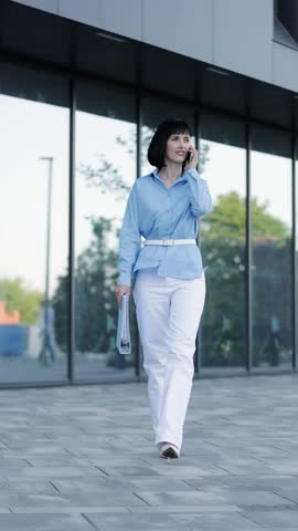 Confident adult businesswoman, boss, entrepreneur or office employe in formal clothes answers on work calls issues and checks documents at folder outdoors on office building background. Career woman. Royalty-Free Stock Footage #3464484563