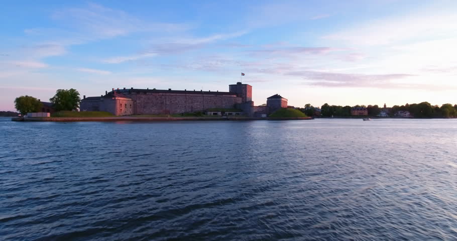 Aerial: A Serene Evening View Of A Historic Stockholm Fortress, With The Swedish Flag Waving Proudly Atop A Stone Tower