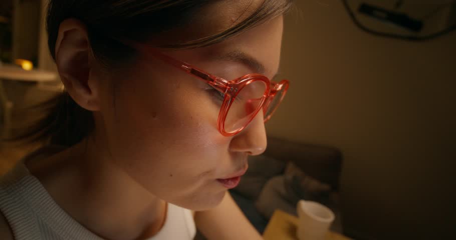 A woman takes off her glasses and rubs her eyes using a laptop sitting at a table at home, close-up of her serious face