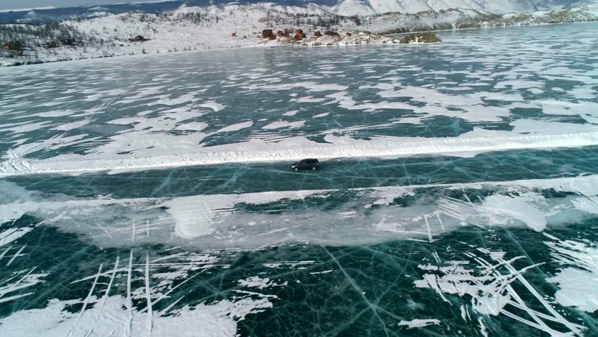Aerial side view on a car driving on an ice road on frozen Baikal. Winter landscape of lake Baikal. Drone follows the car