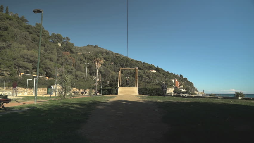 Young boy swinging on a pulley in a playground, approaching from a distance.