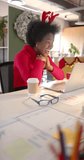 Vertical video of african american casual businesswoman making video call in office, slow motion. Casual office, business, communication, christmas, tradition, celebration and work, unaltered.