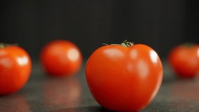 Tomatoes are spread out on the table and more are rolling into the frame. Nice background video with fleshy red vegetables. High quality FullHD footage