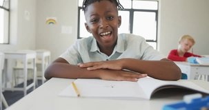 Video of happy african american boy sitting at school desk. primary school education, knowledge and learning concept.