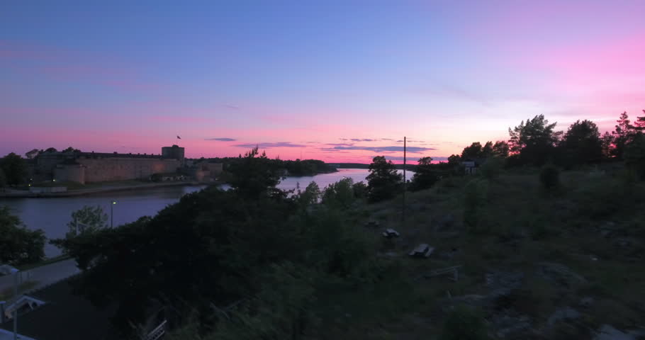 Aerial: The Sun Dips Below The Horizon, Casting A Pink Glow Over A Majestic, Ancient Fortress Standing Guard By The Calm Waters - Stockholm, Sweden