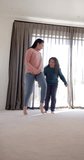 Vertical video of happy biracial mother and daughter dancing and smiling in sunny bedroom. Family, motherhood, wellbeing, relaxation, childhood and togetherness, unaltered.