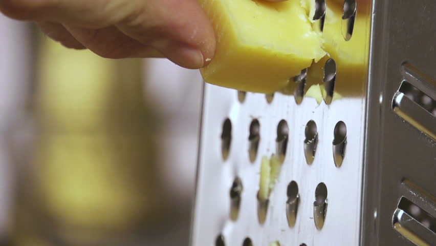 hand grating yellow cheese with a metal grater closeup